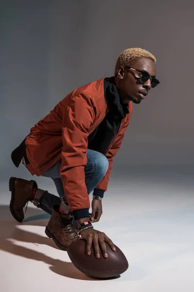 Stylish young african american man holding rugby ball on floor — Stock Photo