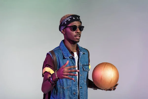 Elegante joven afroamericano hombre sosteniendo pelota de baloncesto de oro aislado en gris — Stock Photo