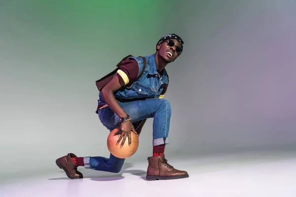 Élégant jeune homme afro-américain jouer avec balle de basket dorée sur gris — Photo de stock