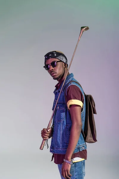 Stylische junge afrikanisch-amerikanische Mann mit goldenem Golfschläger und Blick in die Kamera isoliert auf grau — Stockfoto
