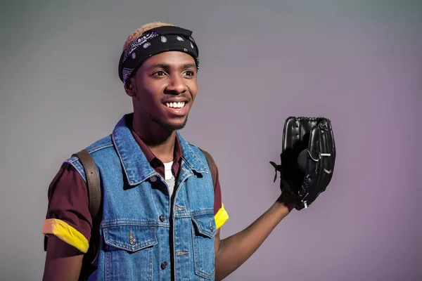 Sonriente joven afroamericano hombre con guante de béisbol mirando hacia otro lado aislado en gris - foto de stock