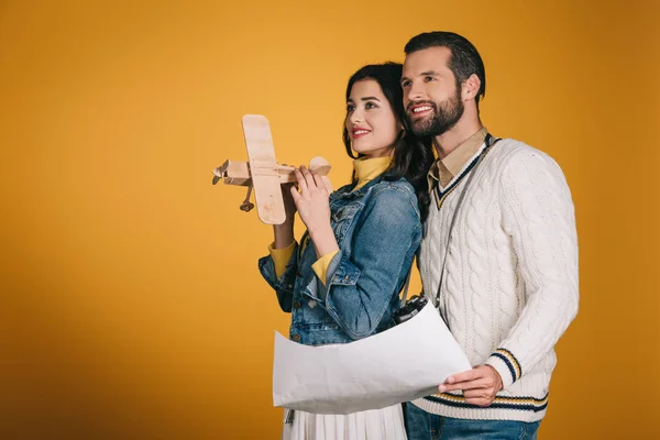 Novia sosteniendo avión de madera y novio sosteniendo mapa aislado en amarillo - foto de stock
