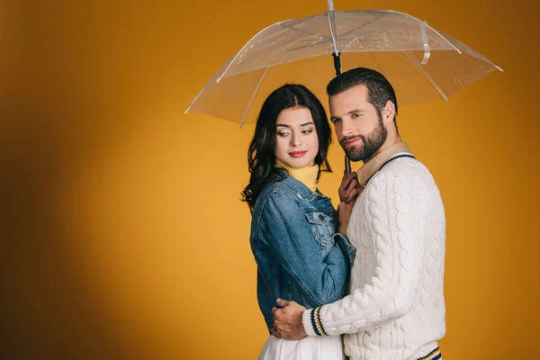 Atractiva pareja con paraguas transparente aislado en amarillo - foto de stock