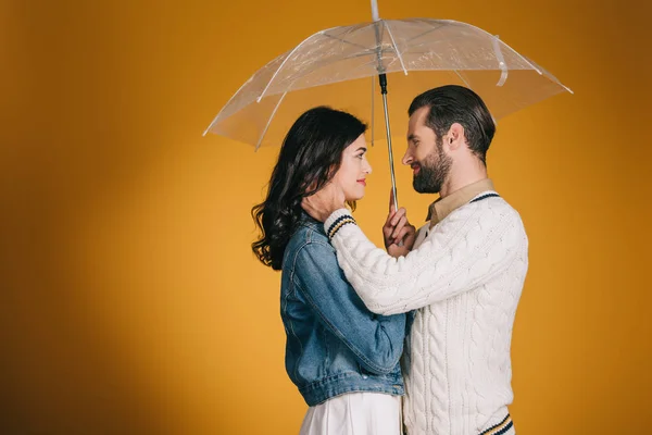 Пара обнимается под прозрачным зонтиком, изолированным на желтый — стоковое фото