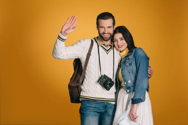 Boyfriend waving hand and hugging girlfriend isolated on yellow — Stock Photo