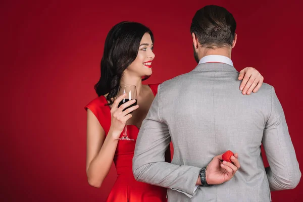 Rückansicht des Freundes versteckt roten Kasten vor Freundin isoliert auf rot — Stockfoto
