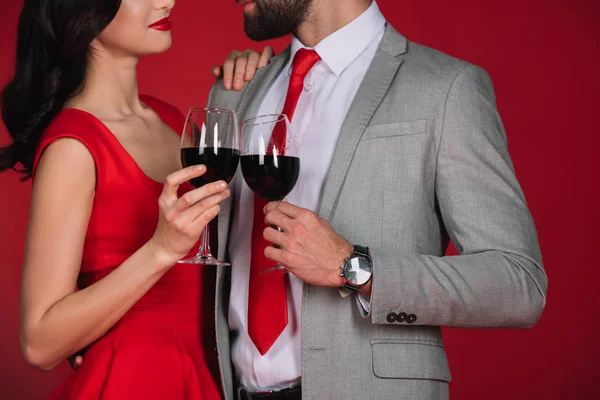 Image recadrée de couple cliquetant avec des verres de vin et se regardant isolés sur rouge — Photo de stock