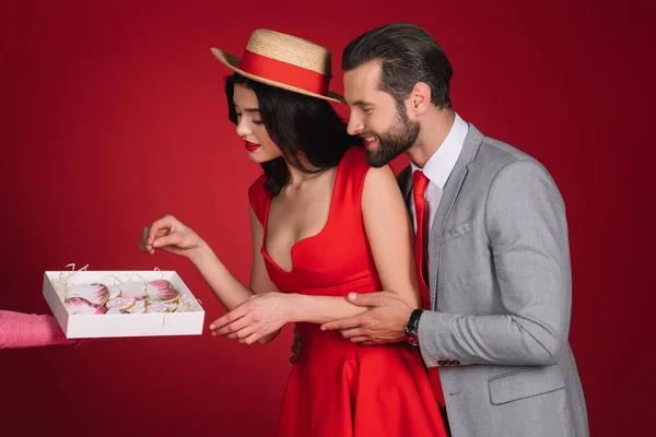 Attraktives Mädchen nimmt herzförmige Kekse isoliert auf rot — Stockfoto