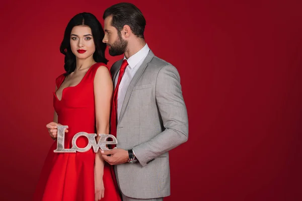 Casal afetuoso de pé com sinal de amor isolado no vermelho — Fotografia de Stock