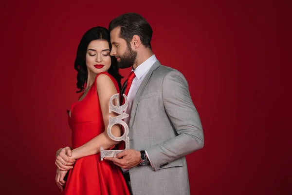 Attractive couple standing with sign love isolated on red — Stock Photo