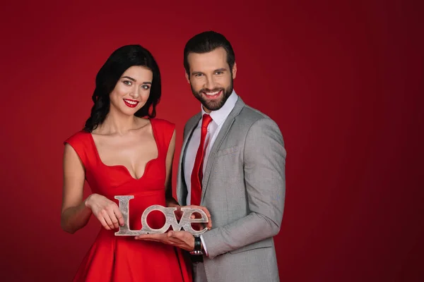 Smiling couple standing with sign love isolated on red — Stock Photo