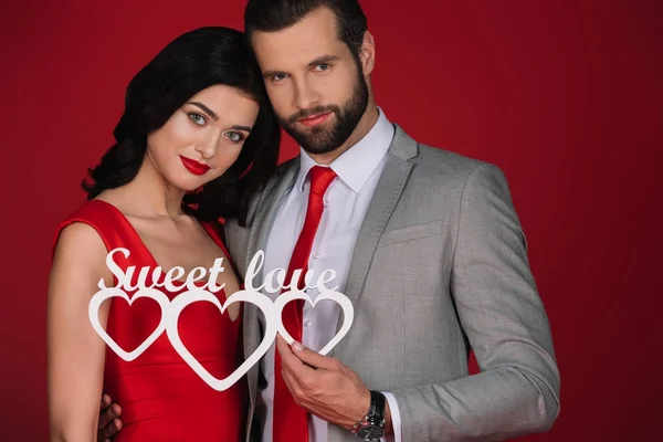 Attraktives Paar mit Schild süße Liebe isoliert auf rot — Stockfoto