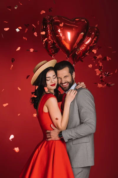 Riendo pareja bajo caída confeti aislado en rojo - foto de stock