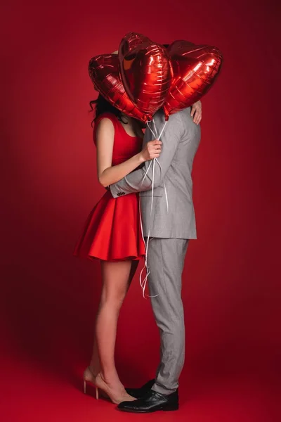 Couple couvrant les visages avec un paquet de ballons sur rouge — Photo de stock