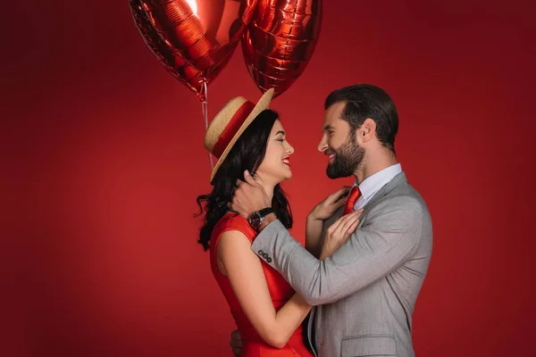 Casal elegante com balões vermelhos olhando um para o outro isolado no vermelho — Fotografia de Stock