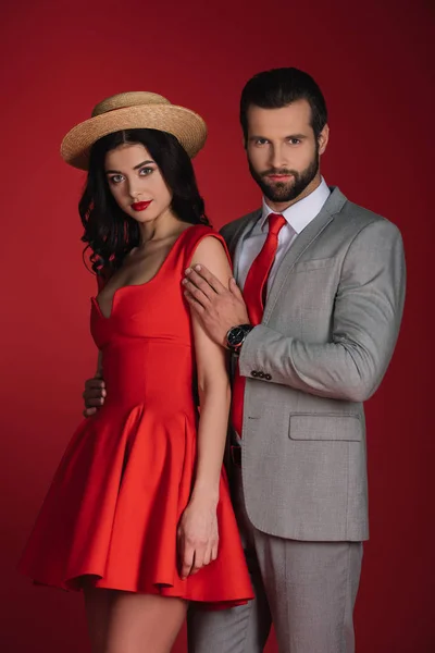 Boyfriend hugging girlfriend and they looking at camera isolated on red — Stock Photo