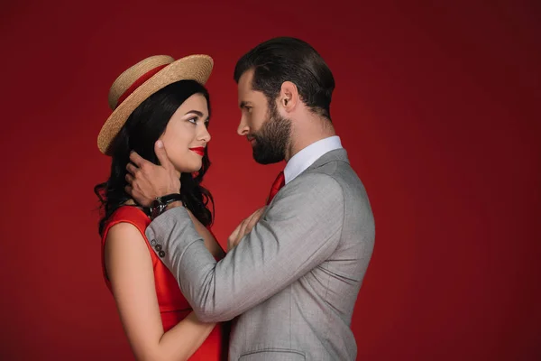 Привлекательная пара обнимается и смотрит друг на друга изолированно на красный — стоковое фото