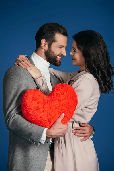 Счастливая улыбающаяся пара, держащая подушку в форме сердца, изолированную на голубом — стоковое фото
