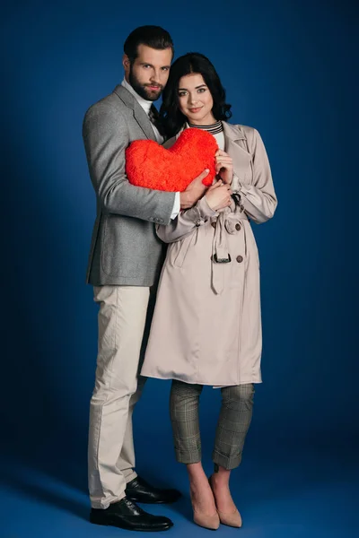 Пара держит подушку в форме сердца и смотрит на камеру на голубом — стоковое фото