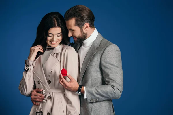 Novio haciendo propuesta a feliz novia aislado en azul - foto de stock