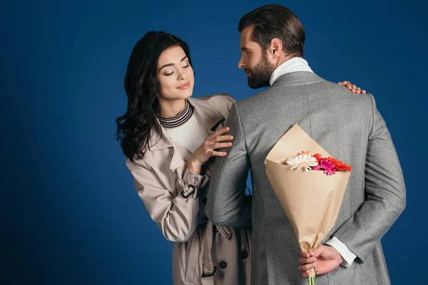Boyfriend hiding bouquet from girlfriend isolated on blue — Stock Photo