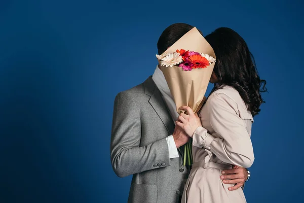 Couple covering faces with bouquet isolated on blue — Stock Photo