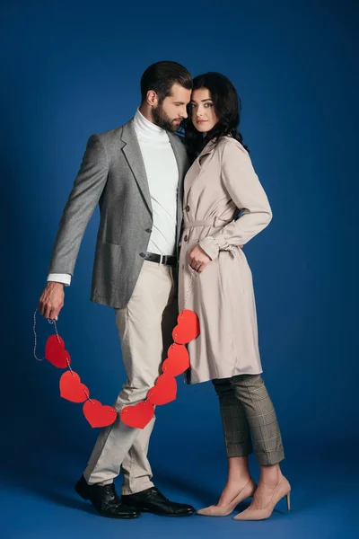Пара, держащая гирлянду из красных сердец и обнимающая синий — стоковое фото