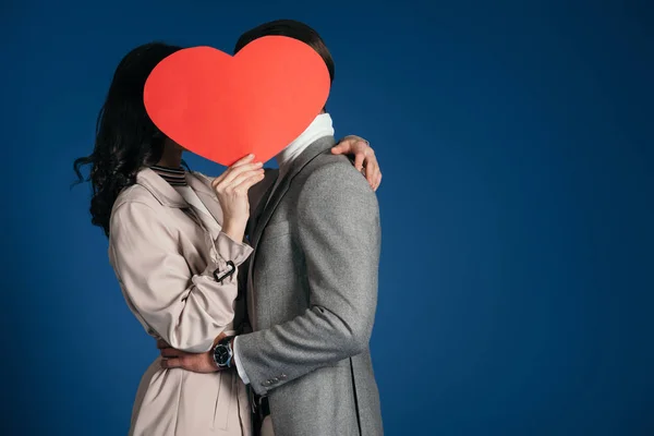 Пара покриває обличчя шматочком паперу у формі серця ізольовані на синьому — стокове фото