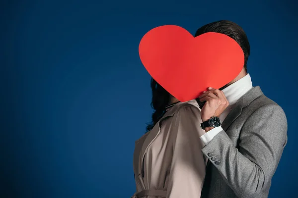 Couple couvrant les visages avec morceau de papier en forme de coeur isolé sur bleu — Photo de stock