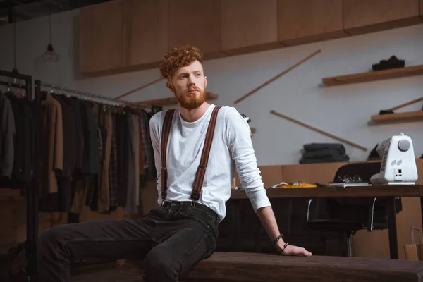 Elegante joven barbudo diseñador de moda mirando hacia otro lado en el taller - foto de stock