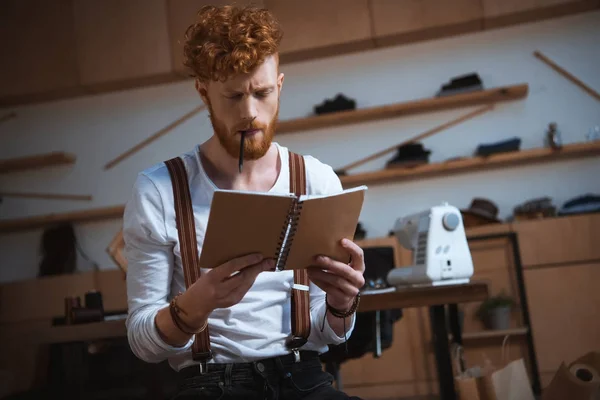 Serious young male fashion designer holding notebook at workplace — Stock Photo