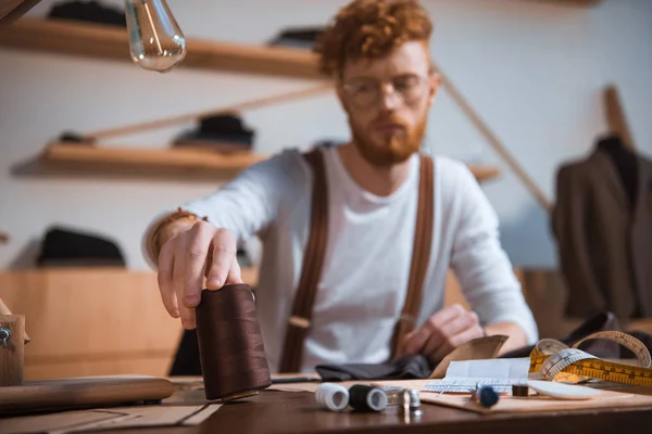 Vista de cerca del joven diseñador de moda masculino que trabaja con hilos en el taller - foto de stock