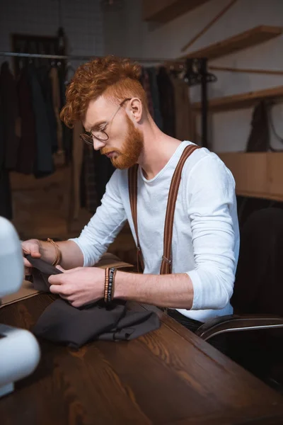 Jeune créateur de mode masculin dans des lunettes tenant tissu à l'atelier — Photo de stock