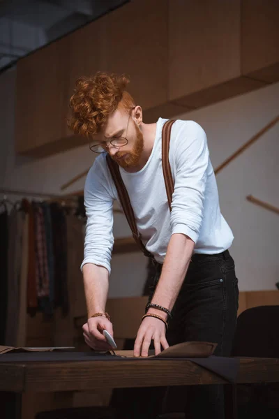 Focused young male fashion designer working working with fabric at workshop — Stock Photo