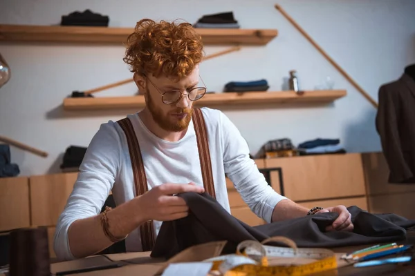 Focalizzato giovane stilista di moda maschile che lavora con tessuto sul posto di lavoro — Foto stock