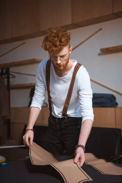 Estiloso jovem designer de moda masculina em óculos trabalhando com padrões de costura e tecido — Fotografia de Stock