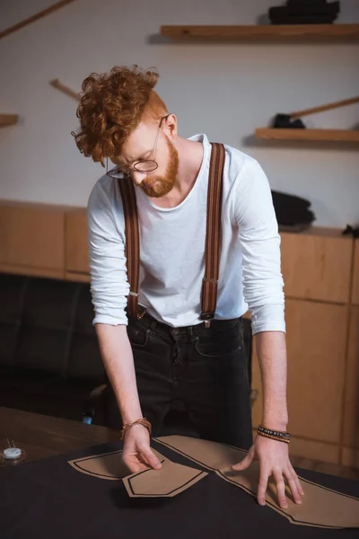 Jovem designer de moda masculina em óculos trabalhando com padrões de costura e tecido — Fotografia de Stock