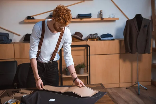 Fokussierte junge männliche Modedesignerin mit Brille, die mit Nähmustern und Stoff arbeitet — Stockfoto