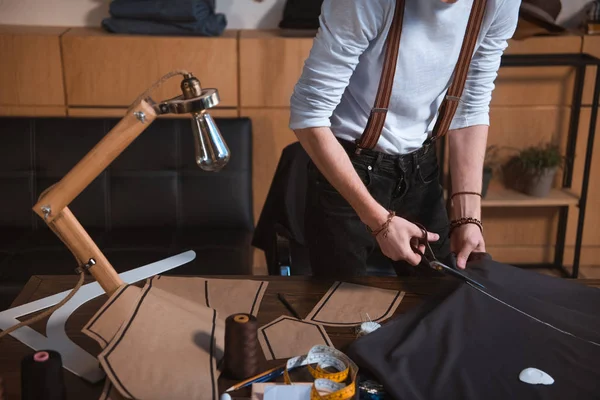 Recortado disparo de joven diseñador de moda masculino trabajando con tijeras y tela en el taller - foto de stock