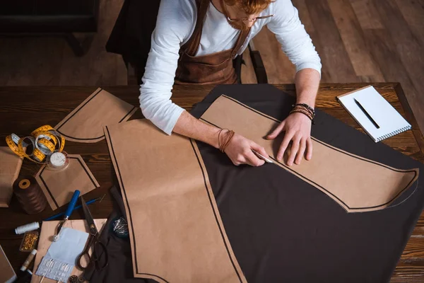 Schnappschuss eines bärtigen männlichen Modedesigners, der am Arbeitsplatz mit Schnittmustern, Werkzeugen und Stoff arbeitet — Stockfoto