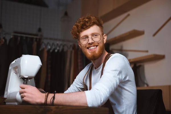 Beau jeune créateur de mode souriant travaillant avec machine à coudre — Photo de stock