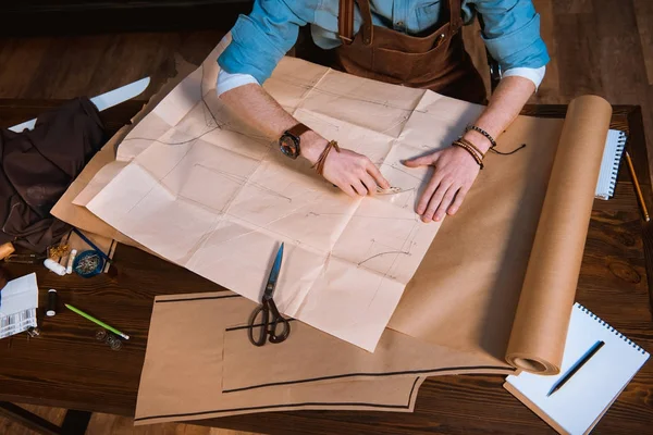 Schnappschuss eines männlichen Modedesigners in Schürze, der am Arbeitsplatz Schnittmuster herstellt — Stockfoto