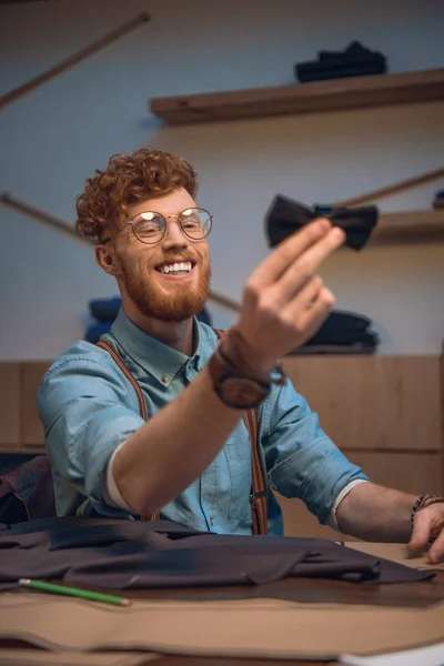 Smiling young male fashion designer in eyeglasses holding black bow tie — Stock Photo