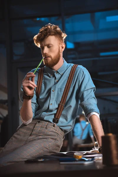 Stylische junge Modedesignerin in Hosenträgern am Tisch am Arbeitsplatz — Stockfoto