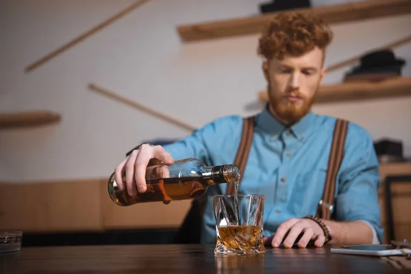 Vista de cerca del joven que vierte whisky de la botella en vidrio - foto de stock