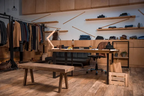 Studio de design de vêtements intérieur avec des vêtements élégants sur les cintres et bouteille de whisky sur la table — Photo de stock