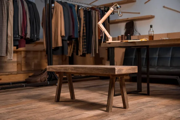 Local de trabalho designer de moda com roupas elegantes em cabides e garrafa de uísque na mesa — Fotografia de Stock