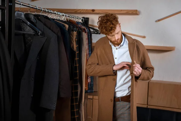 Schöner junger Mann in braunem Mantel in Boutique — Stockfoto