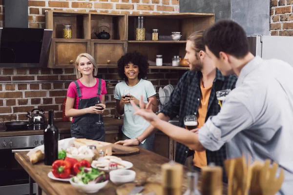 Men looking at multiethnic female friends in kitchen — Stock Photo