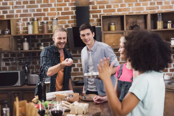 Amigos multiétnicos jugando con huevos de pollo en la cocina — Stock Photo
